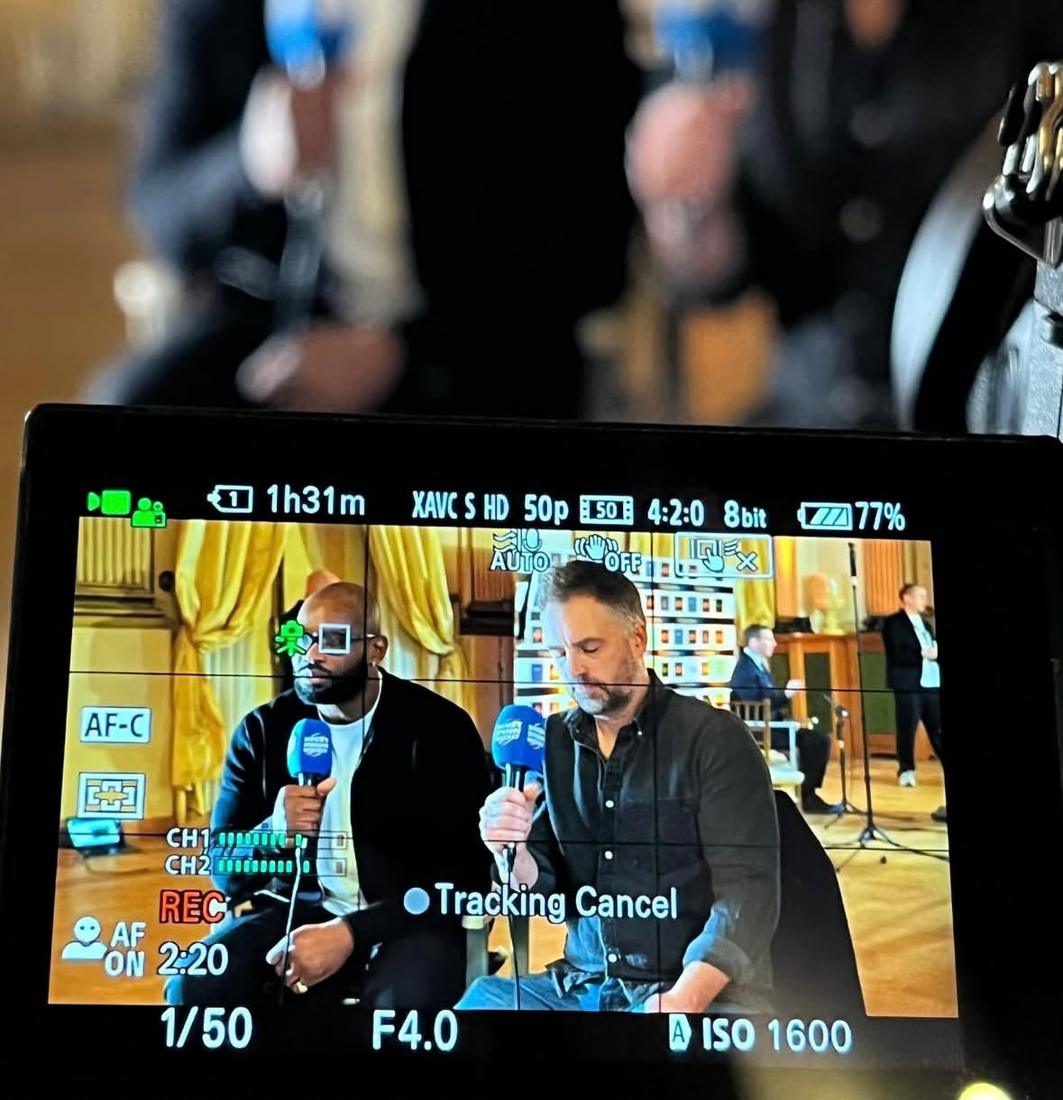 A camera monitor showing Chris filming an interview