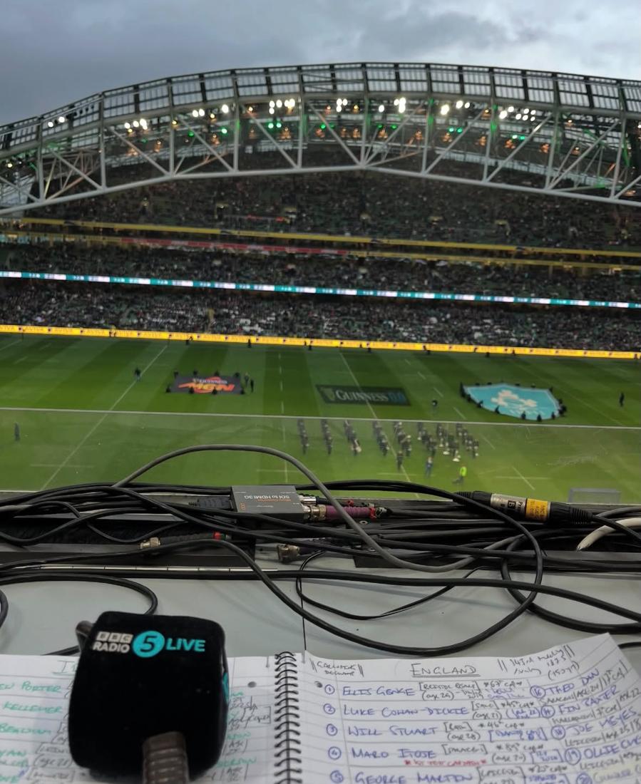 View from the commentary position over a packed stadium, with notes and a 5 Live microphone