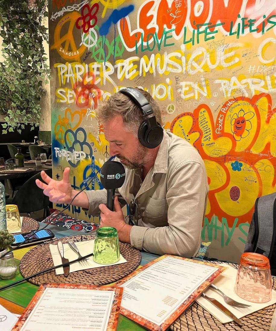 Chris recording the podcast in a colourful café, microphone and headphones on